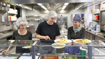 Drei Frauen bei der Speiseausgabe an der Theke einer Großküche. Foto: Bernd Wackerbauer