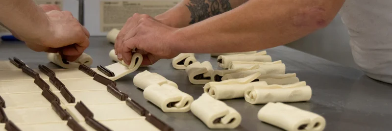 Zwei Hände, die Croissant-Teig mit Schokolade füllen.