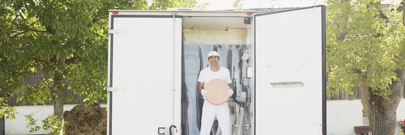Mann vor dem Laderaum eines LKW mit einem Laib Käse in der Hand.