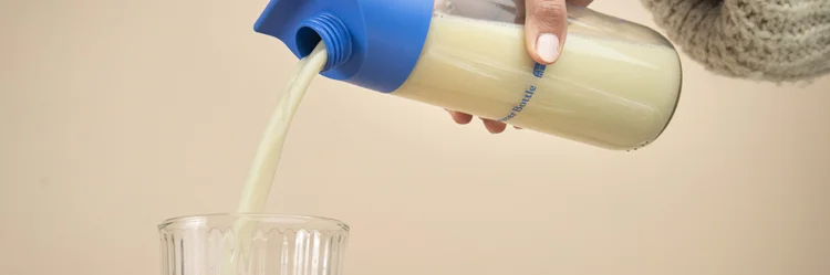 Eine Hand mit einer Flasche, die Hafermilch in ein Glas schüttet.