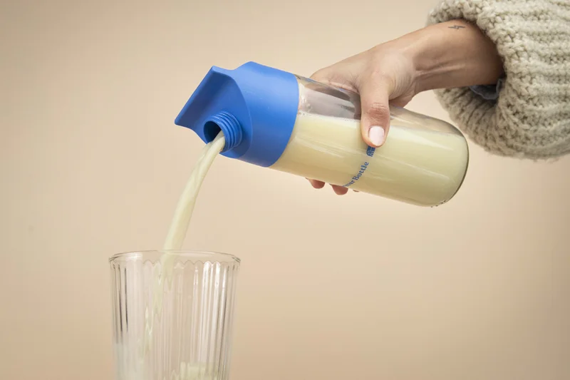 Eine Hand mit einer Flasche in der Hand, die Hafermilch in ein Glas schüttet.