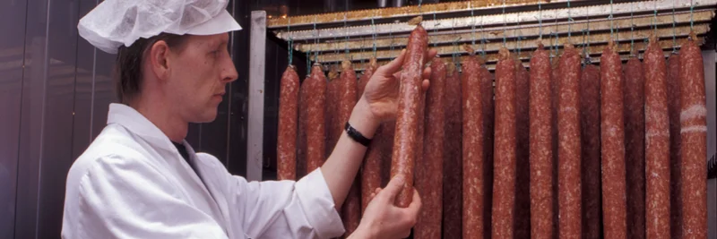 Metzger steht vor einem Wurstregal.