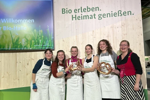 Sechs junge Frauen präsentieren lächelnd Brezeln. Im Hintergrund ist der Schriftzug "Bio erleben. Heimat genießen." zu sehen.
