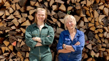 Zwei Frauen stehen vor geschichteten Holzscheiten.