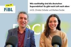 Eine Frau und ein Mann sitzen vor einem Mikro und schauen freundlich in die Kamera. Klick führt zu Großansicht.