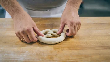 Hände, die einen Brezel-Teigling kneten.