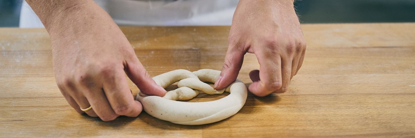 Hände, die einen Brezel-Teigling kneten.