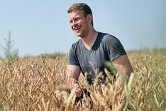Mann sitzt in einem Lupinenfeld. Er lacht. Klick führt zu Großansicht.