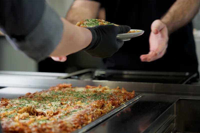 Essensausgabe: Hand reicht Essen über Theke. Klick führt zu Großansicht in neuem Fenster.