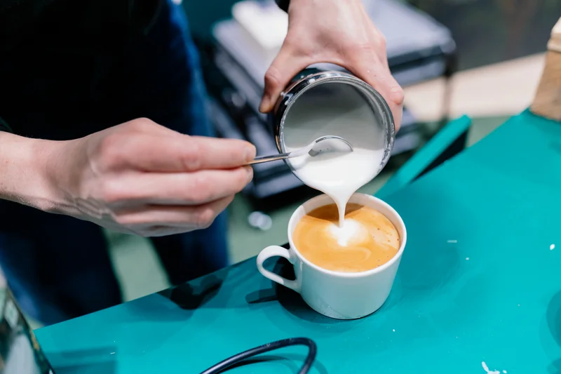 Aufgeschäute Milch wird in eine Kaffeetasse gegeben. Klick führt zu Großansicht.