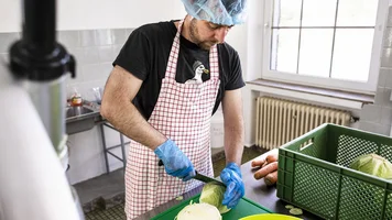 Ein Mann mit Schürze und Haarnetz beim Schneiden von Kohl.