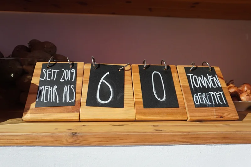 Aufsteller aus Holz mit der Aufschrift: "Seit 2019 mehr als 60 Tonnen gerettet". Klick führt zu Großansicht in neuem Fenster.
