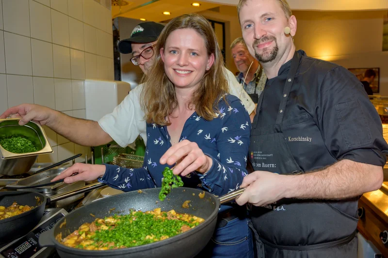 Mann und Frau beim Kochen mit großer Pfanne. Klick führt zu Großansicht im neuen Fenster.