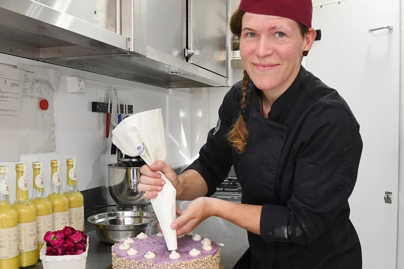 Eine Konditorin in schwarzem Gewand beim Verzieren einer Torte. Klick führt zu Großansicht.
