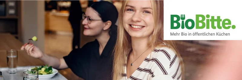 Zwei Frauen sitzen an einem Tisch und essen gemeinsam in einer Kantine.