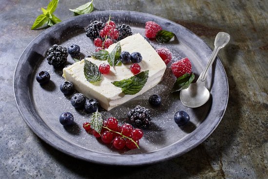 Wildblütenhonigparfait mit geeister Minze und frischen Beeren angerichtet auf einem Teller mit frischen Beeren.