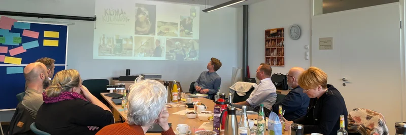 Menschen sitzen um einen Tisch und begutachten eine an die Wand projizierte Grafik.