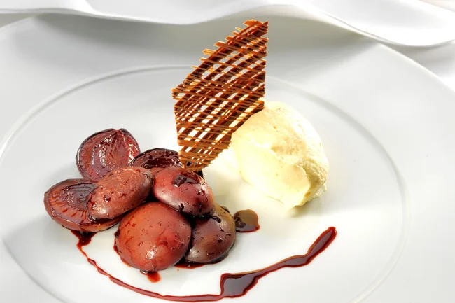 Weißes Schokoladen-Lebkuchen-Mousse mit Rotweinzwetschgen angerichtet auf einem Teller.