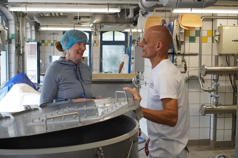 Mann und Frau stehen in einer Käserei neben einem großen Bottich.