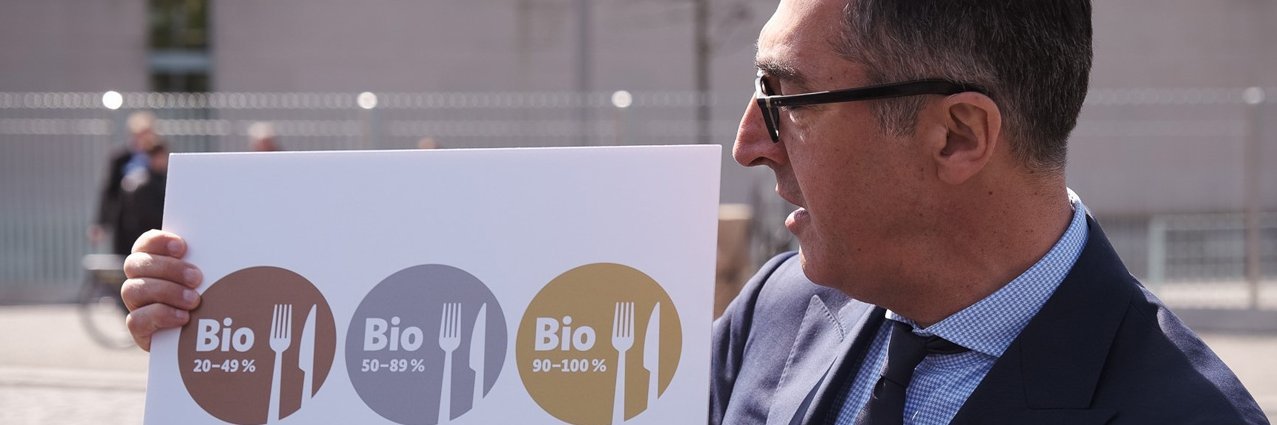 Bundesminister Cem Özdemir zeigt die drei neue Bio-Zeichen für die Außer-Haus-Verpflegung.