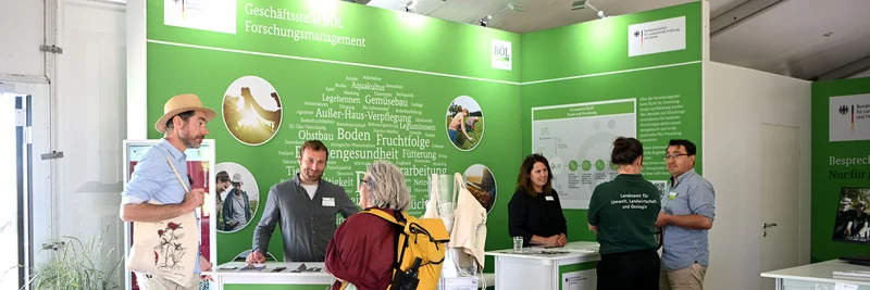 Männer und Frauen stehen an Infotischen auf einer Messe