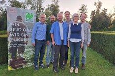 Fünf Männer und eine Fraue lachen in die Kamera. Neben ihnen steht Plakat mit dem Naturland-Schriftzug darauf. Klick führt zu Großansicht.