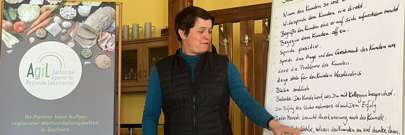 Frau steht neben einem Whiteboard, auf das sie zeigt.