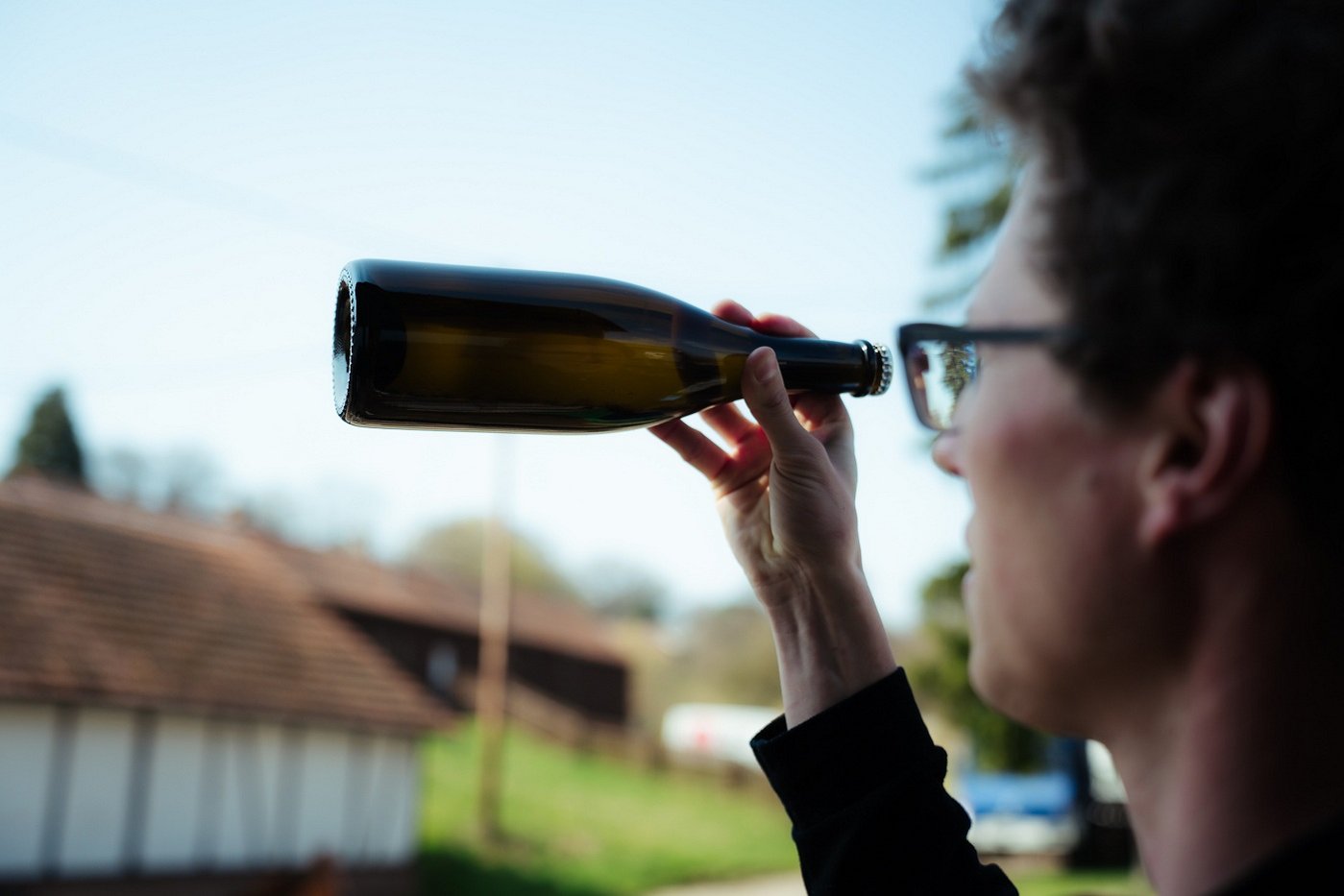Ein Mann wie er eine Fasche Wein in der Hand hält und sie im Licht begutachtet. Klick führt zu Großansicht.