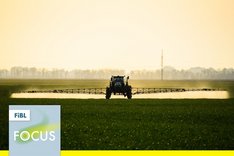 Ein Traktor, der Mittel auf einem Feld ausbringt. Im linken unteren Bildrand ist ein Quadrat in dem steht "FiBL Focus". Klick führt zu Großansicht.