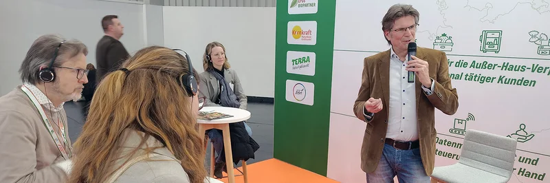 Mann mit Mikro vor einem Publikum. 