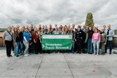 Eine Gruppe Menschen, die in die Kamera schaut. Die vorderen Menschen halten einen Banner hoch auf dem "Bio verarbeiten – Praxis-Netzwerk" steht. Klick führt zu Großansicht.