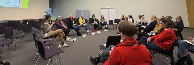 Frauen sitzen in einem Stuhlhalbkreis und diskutieren.