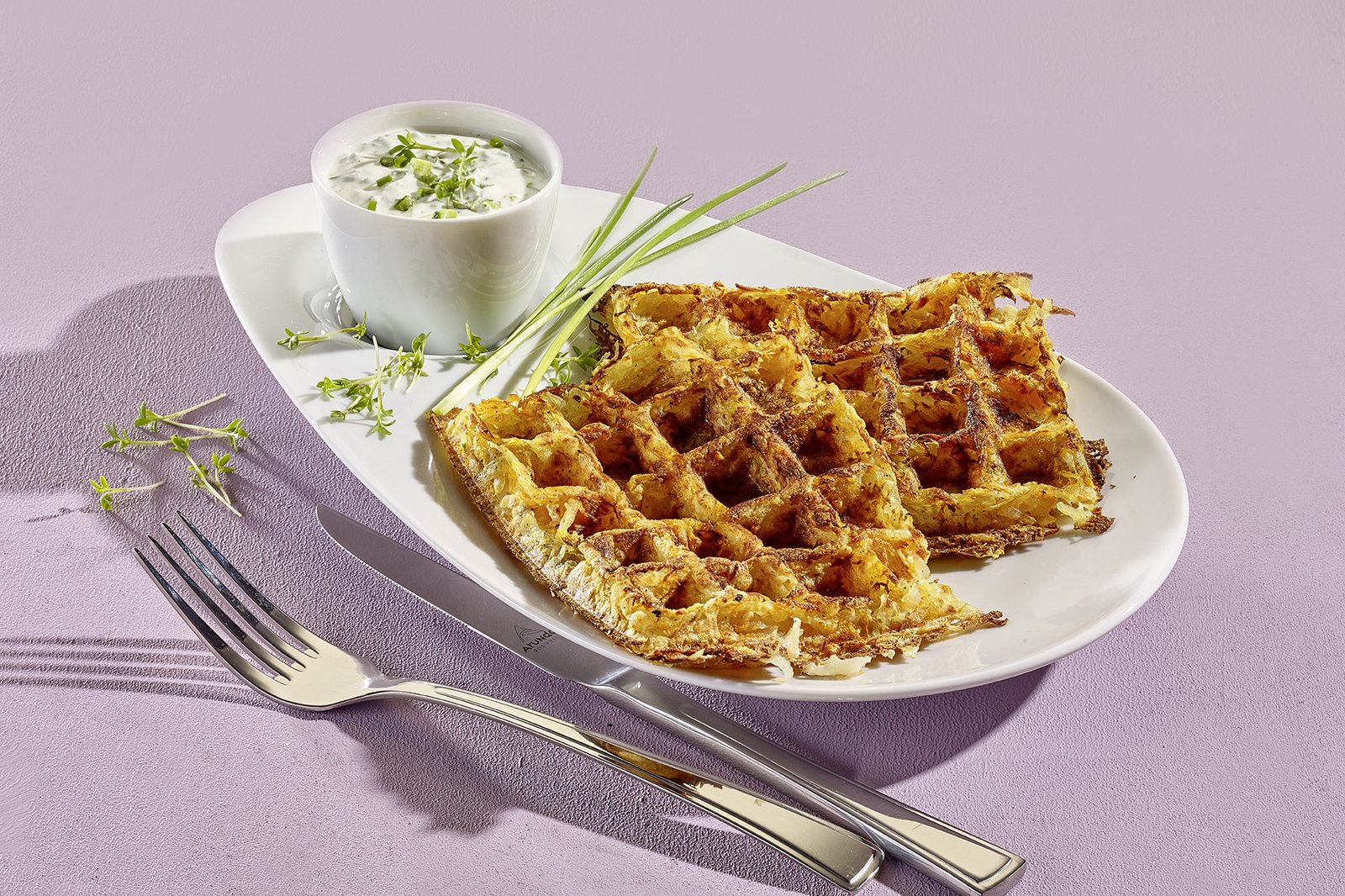 Kartoffel-Möhren-Waffeln mit Kräuterquark, Kresse und Schnittlauch auf einem weißen Teller