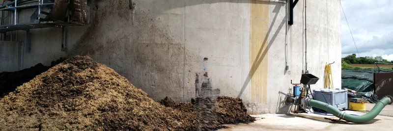 Bild eines Fermenters einer Biogasanlage, vor dem ein Misthaufen liegt.