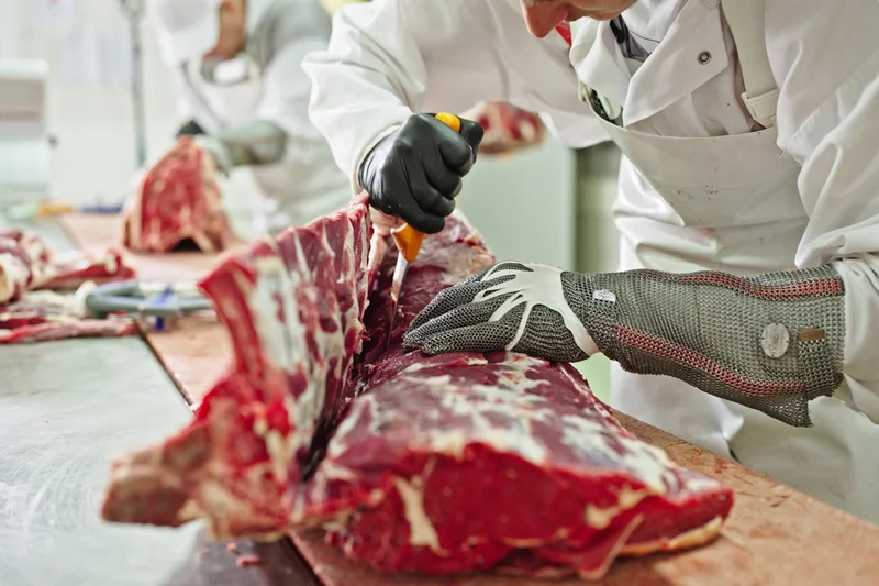 Fleisch auf einem Tisch, das gerade mit Messer zerlegt wird. Klick führt zu Großansicht in neuem Fenster.