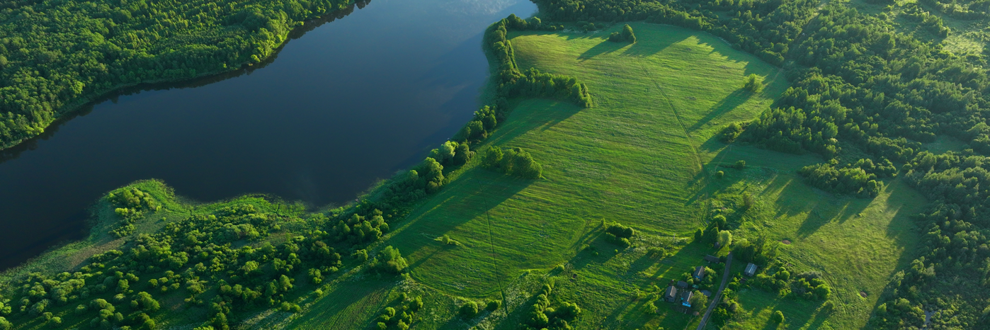 Luftaufnahme eines Sees, an dessen Ufer Wälder und grüne Felder liegen.
