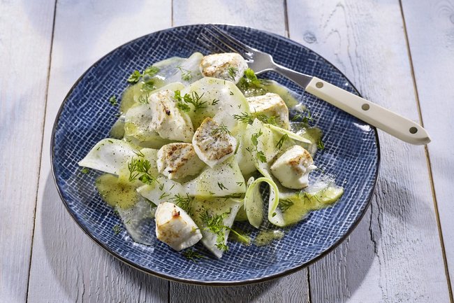 Gehobelter Kohlrabi mit Apfelessig-Holunder Vinaigrette und Ziegenkäse angerichtet auf einem Teller.