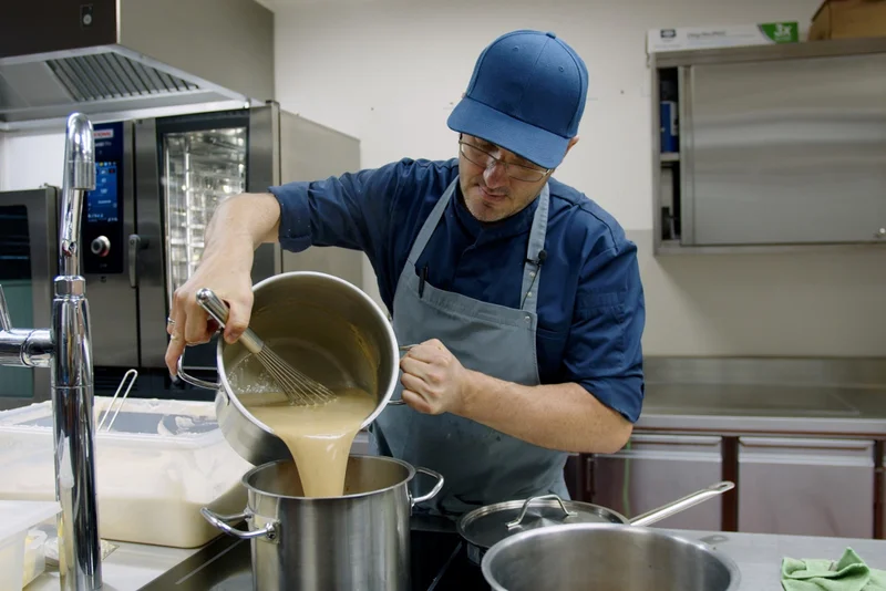 Bernhard Muxel, Küchenchef der Schulküche Lingenau, gießt Suppe von einem Topf in den anderen.