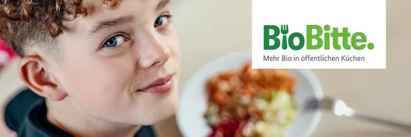 Ein Kind sitzt vor einem Teller mit Essen und schaut in die Kamera.