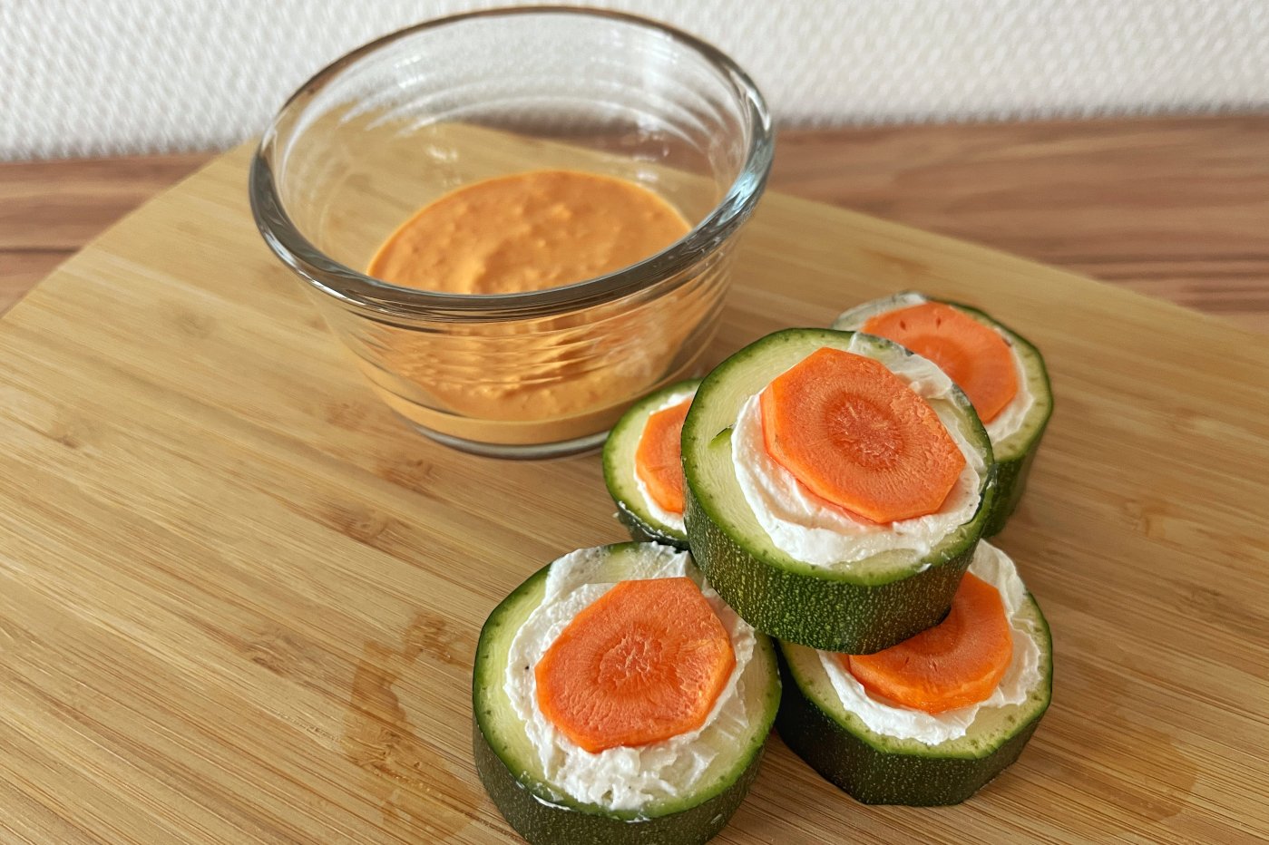 Zucchiniröllchen mit pikanter Ziegenkäsefüllung und Paprika-Dip auf einem Holzbrett serviert.