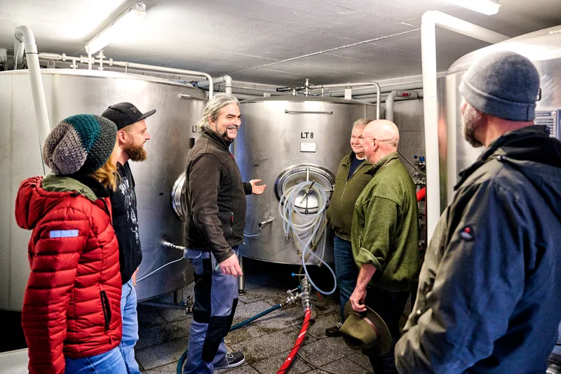 Eine Gruppe steht vor Metalltanks einer Brauerei. Klick führt zu Großansicht in neuem Fenster.