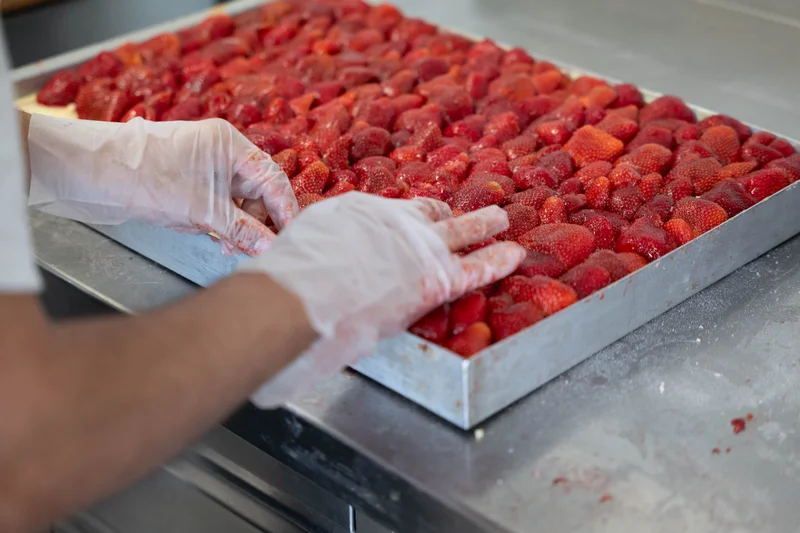 Hände, wie sie Erdbeeren auf einen Erdbeerkuchen legen. Klick führt zu Großansicht.