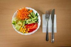 Beilagensalat mit Messer und Gabel auf einem Holztisch.