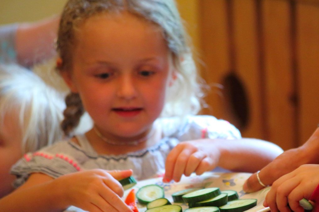 Kinder greifen nach Gurkenscheiben auf einem Teller.