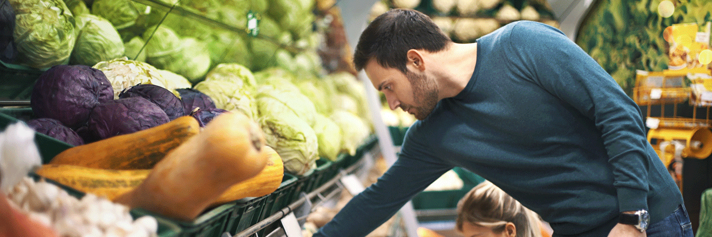 Mann greift in die Gemüsetheke eines Supermarktes.
