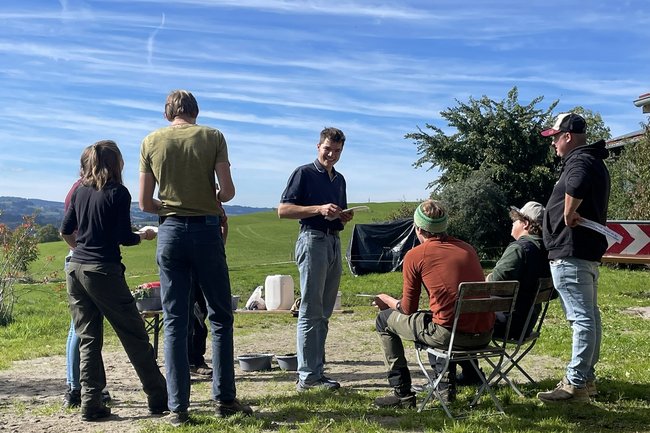 Eine Gruppe junger Menschen steht in einem Feld und diskutiert.