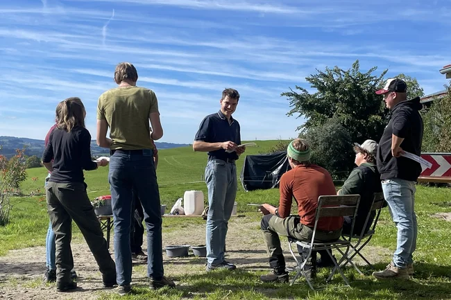 Eine Gruppe junger Menschen steht in einem Feld und diskutiert.