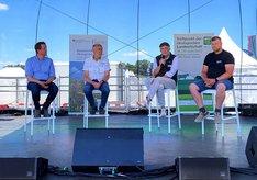 Vier Männer auf Stühlen sitzend auf einer Bühne während einer Podiumsdiskussion.