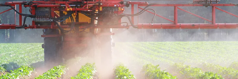Traktor bringt mit Pflanzenschutzspritze Pflanzenschutzmittel mit PFAS aus.