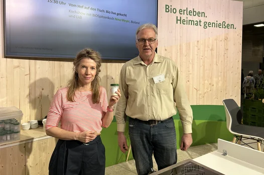 Eine Frau und ein Mann schauen in die Kamera. Die Frau hält ein Glas mit Schraubverschluss in der Hand.